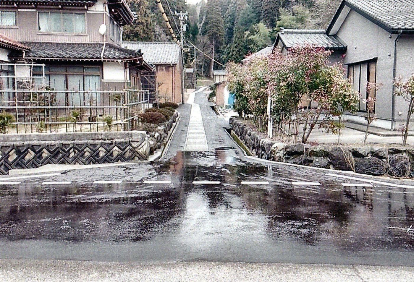 集落の中の道路と坂を上るコンクリート水路